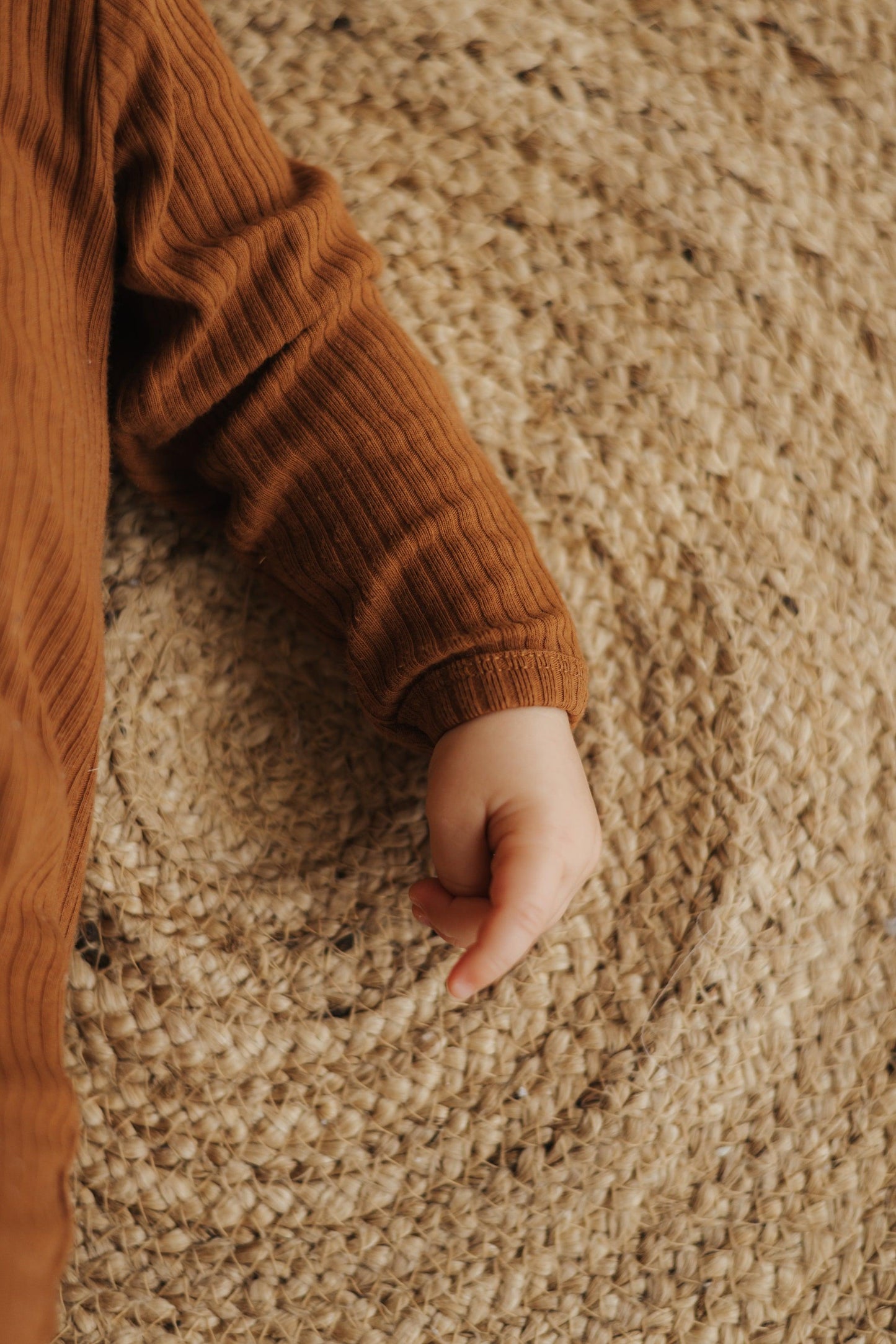 Baby wearing brown ribbed SOALSA Spalni Pajaci za Dojenčke sleep romper lying on woven mat