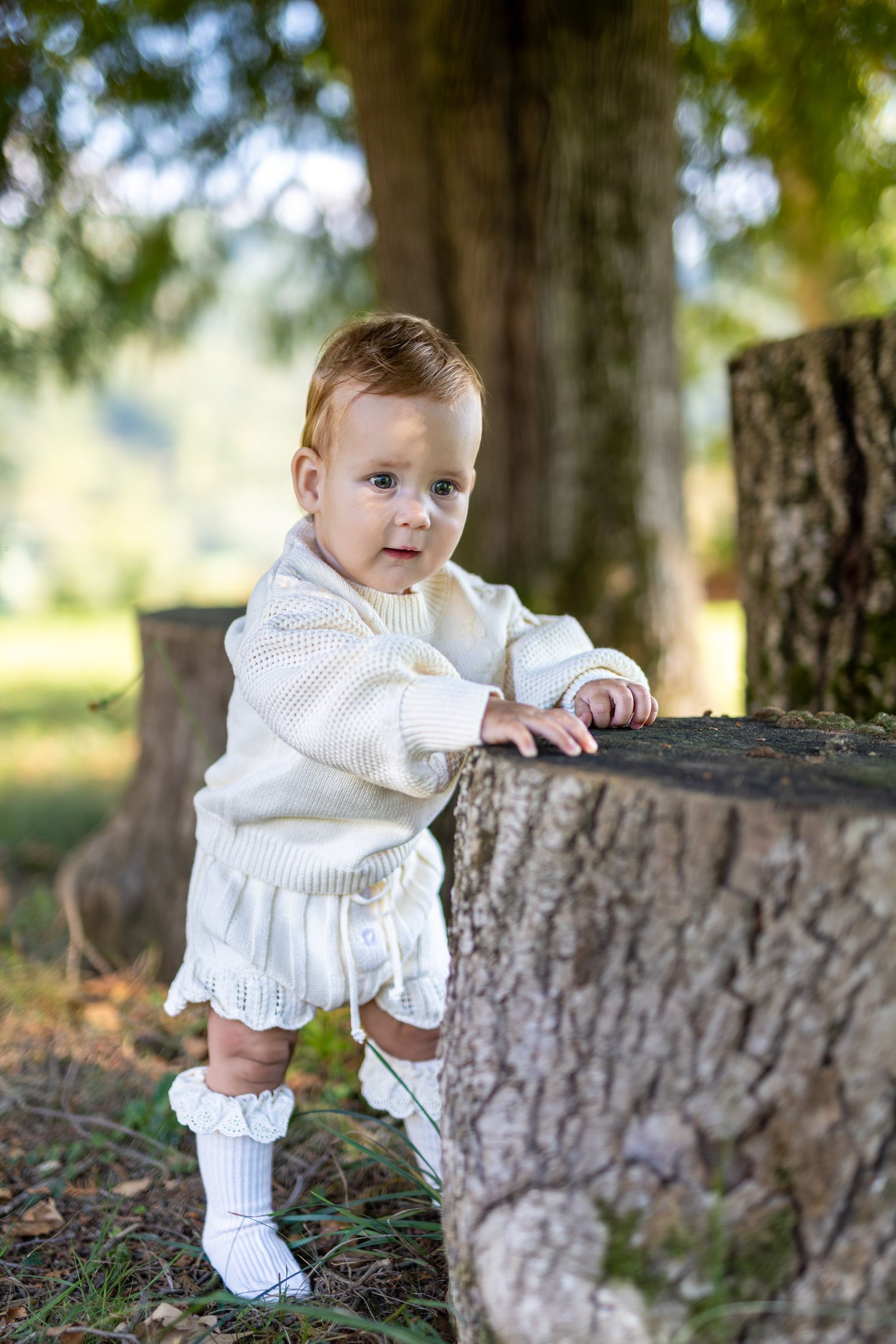 Smiling baby sitting in a cozy chair wearing a white knitted outfit Zimski komplet za novorojenčka for winter