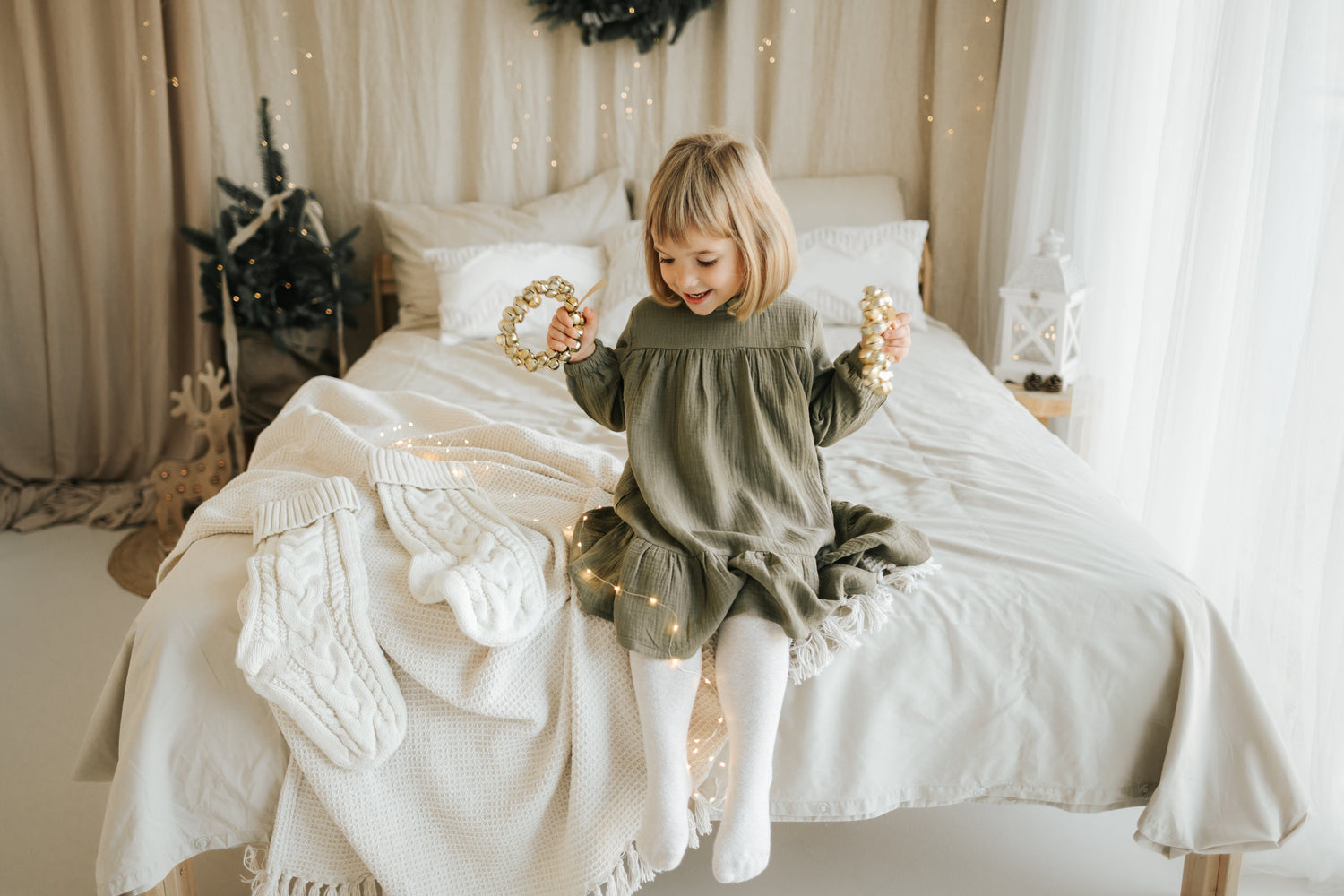 Child sitting on bed wearing Božične obleke za dojenčke green dress with festive holiday decor.SOALSA