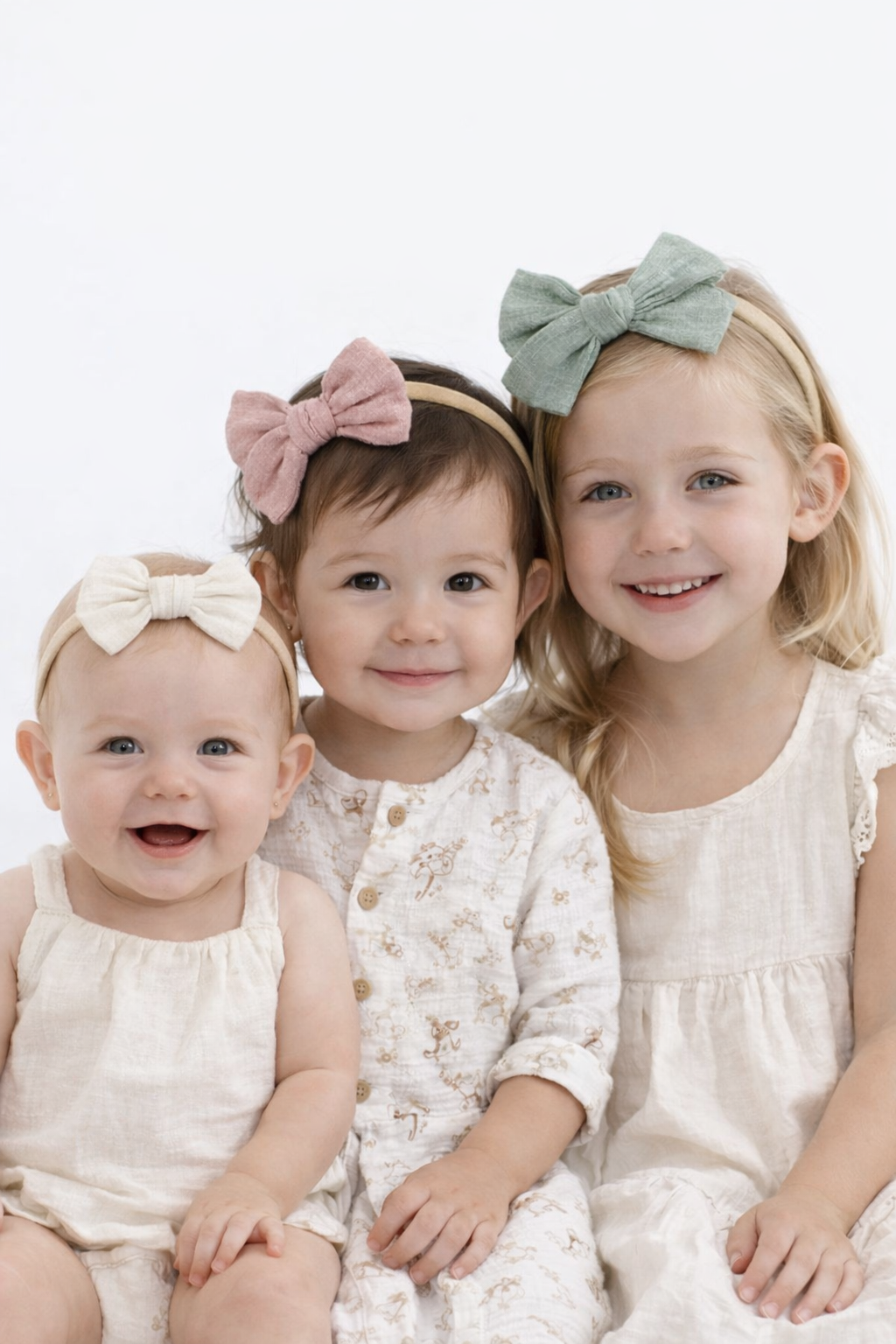Three young children wearing headbands and smiling against a white background