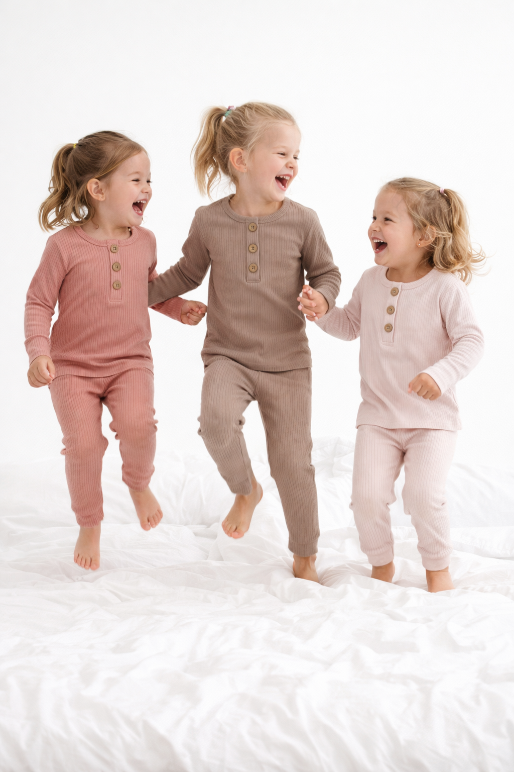 Three children in matching pajamas laughing on a white surface