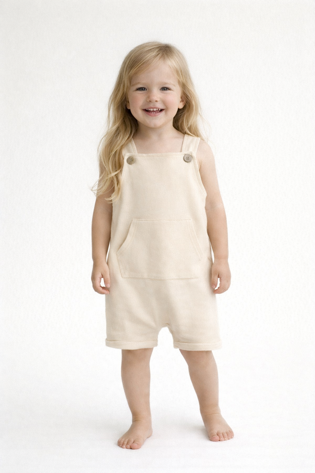 Young girl wearing a beige pinafore dress on a white background