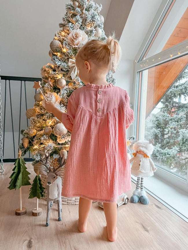 Toddler girl wearing pink Božična obleka za dojenčke standing near decorated Christmas tree by window