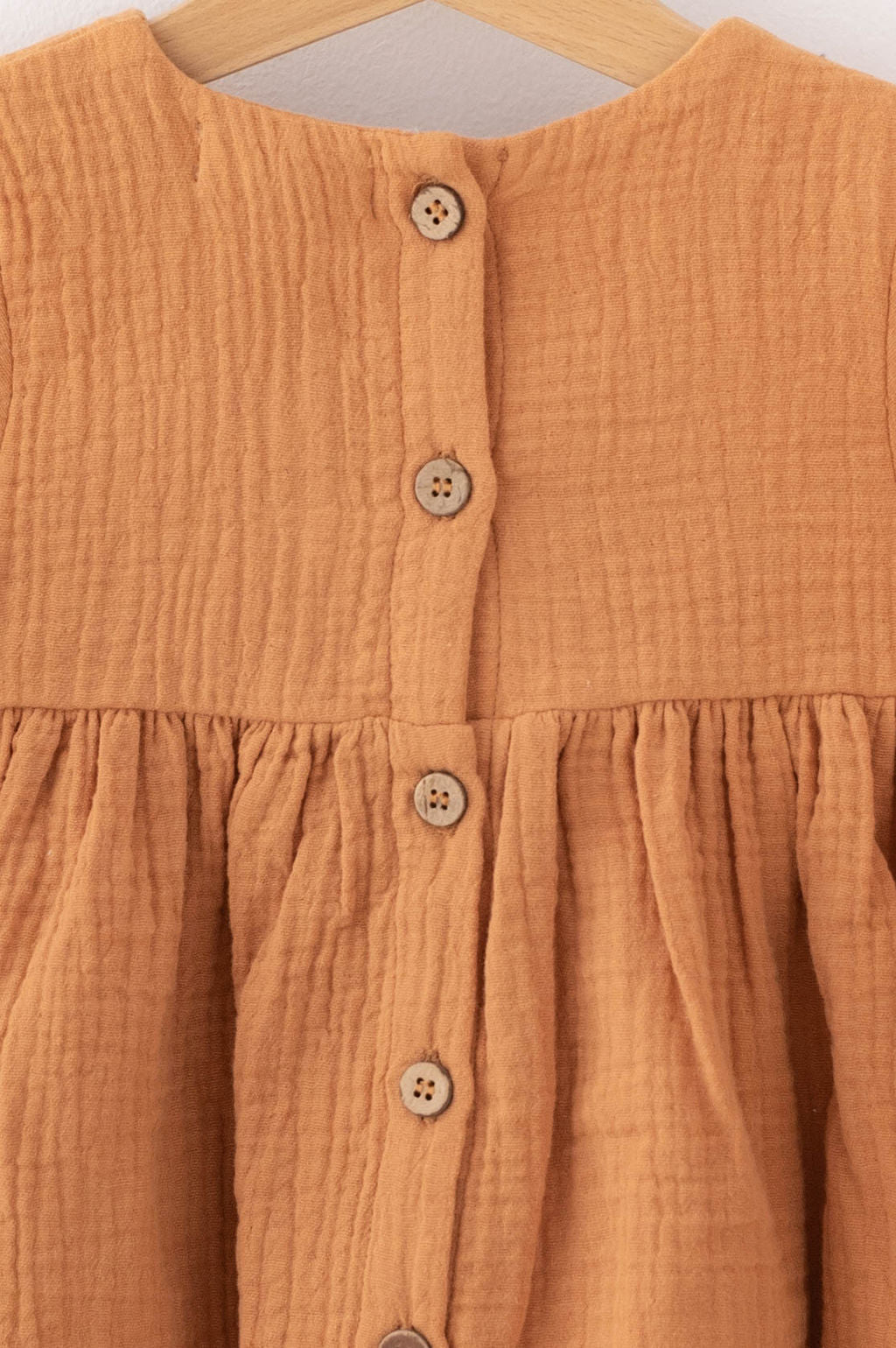 Close-up of brown textured fabric dress with wooden buttons by SOALSA Božična obleka za deklice