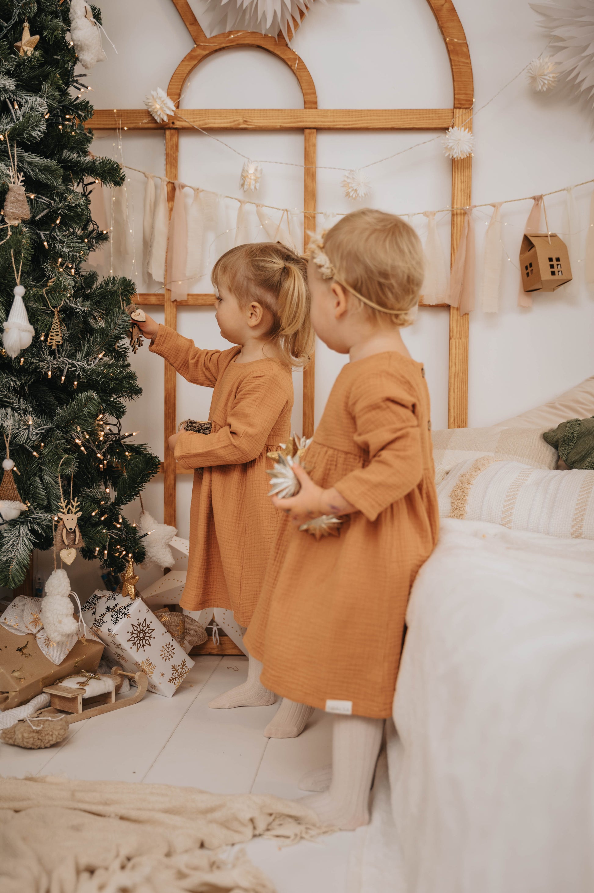Two girls wearing SOALSA Božična obleka za deklice decorating a Christmas tree indoors