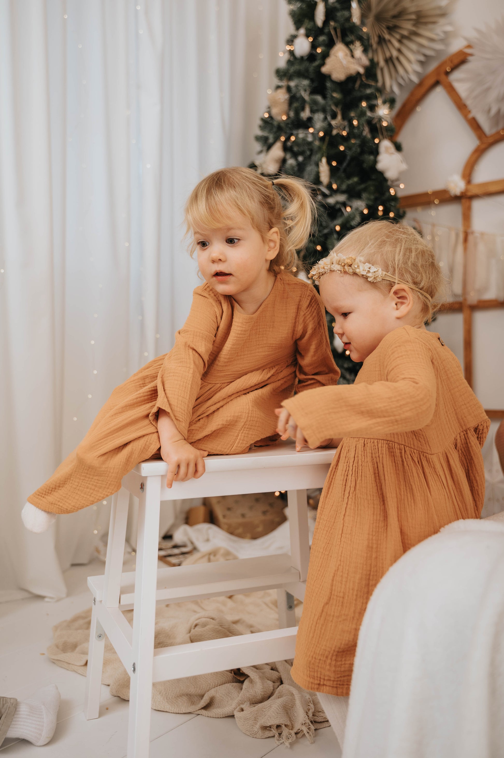 Two toddlers wearing brown Božična obleka za deklice dresses in a cozy holiday setting with a Christmas tree