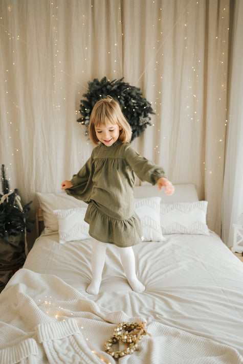 Child wearing SOALSA muslin dress in cozy room with Christmas decorations Božične obleke za otroke