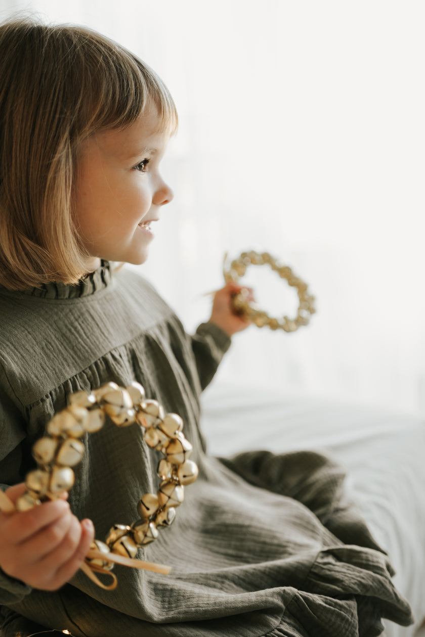 Child wearing muslin dress by SOALSA holding jingle bells for Božične obleke za otroke Christmas celebration