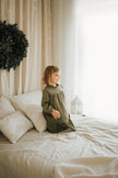 Child wearing SOALSA muslin dress sitting on bed with Christmas decor Božične obleke za otroke