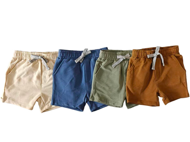 Four pairs of children's shorts in beige, blue, green, and brown on a gray floor.