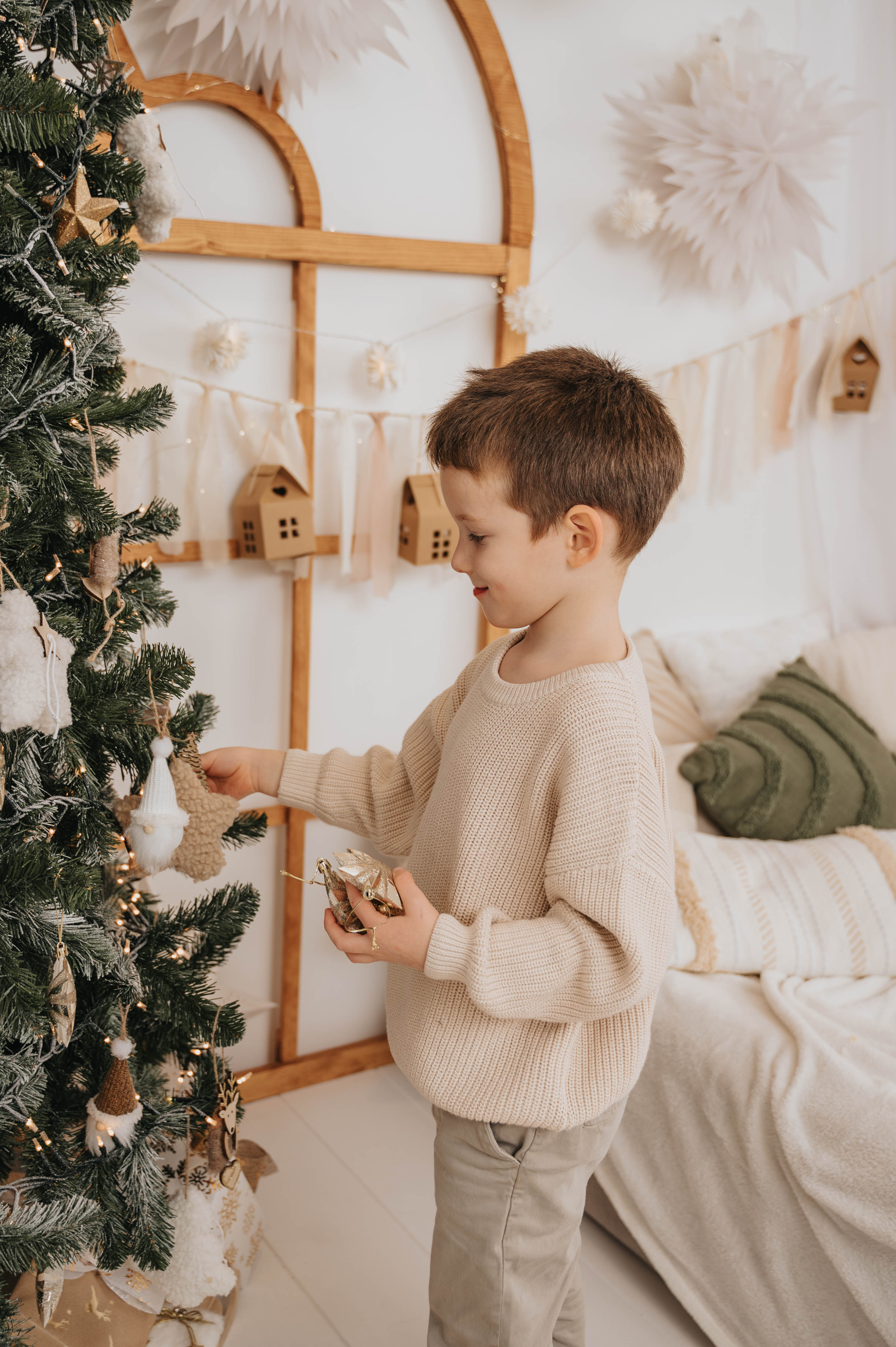 Young boy decorating Christmas tree wearing cozy beige sweater for božični puloverji za otroke