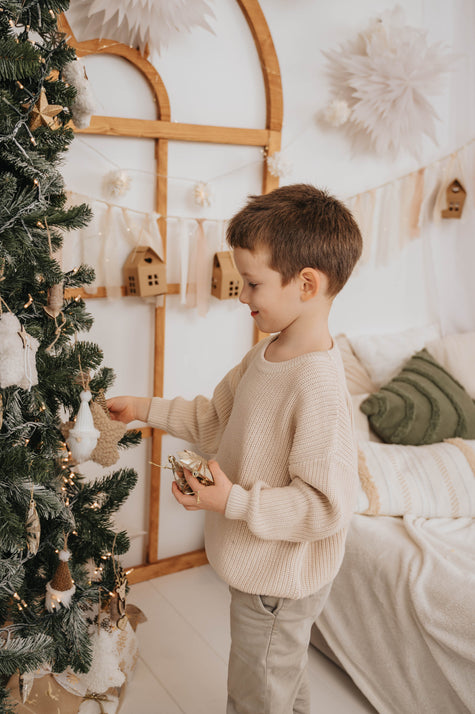 Young boy decorating Christmas tree wearing cozy beige sweater for božični puloverji za otroke