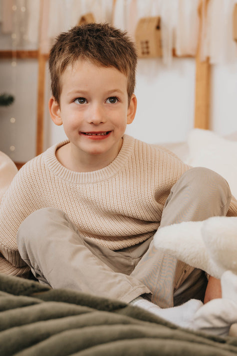 Young boy wearing a beige knit sweater sitting comfortably indoors božični puloverji za otroke