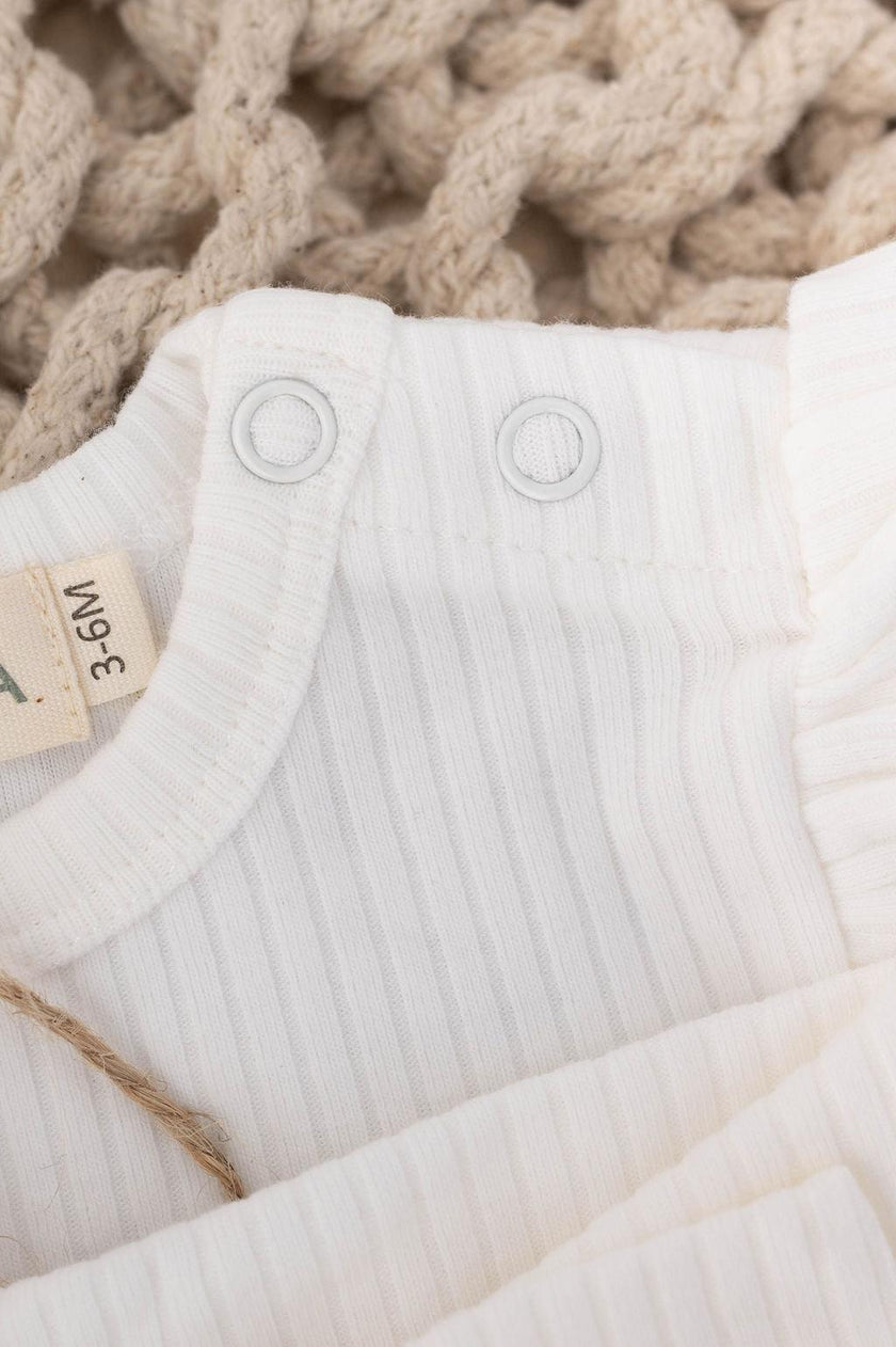 Približen posnetek belega rebrastega bombažnega otroškega kompleta z zapenjanjem na pritiskače iz SOALSA – Komplet za novorojenčka.
